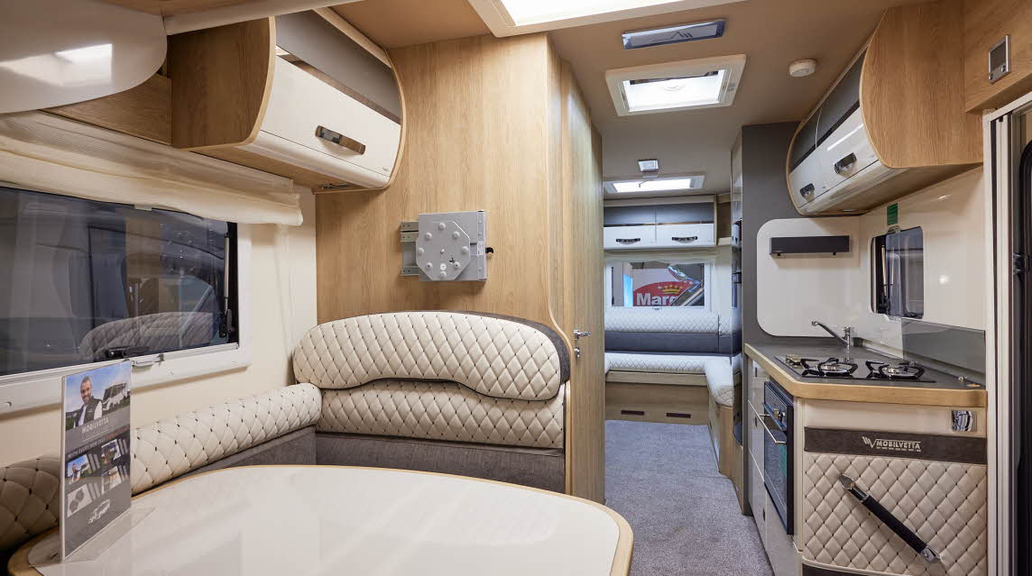 Mobilvetta Tekno Line K-Yacht 95 has two tone grey and cream embossed upholstery.  There are two tone overhead lockers. The floor has a grey carpet.  Towards the rear of the vehicle there is a rear lounge.