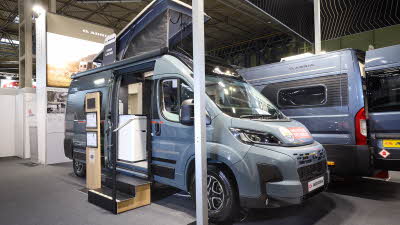 The Adria Twin Sport has a grey exterior. The habitation door is open and there are two steps to gain easy access. There is an information board to the left of the steps. The rising roof is open.