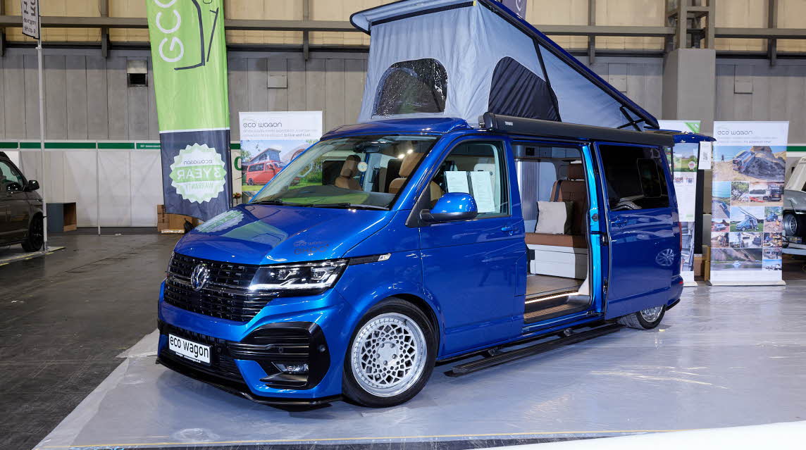 Ecowagon Expo+ exterior the campervan is royal blue and the sliding door is open showing into the interior, the rising roof is fully open showing grey canvas and three windows.