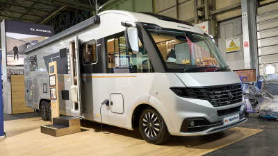 Adria Supersonic’s exterior is silver and black, the entrance door is open and there are wooden steps to gain easy access.  There is an interactive information board by the side of the van.