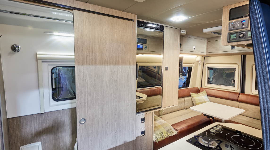 RP Motorhomes Rebel AWD U has two tone copper and cream upholstery.  There are wooden overhead lockers. There is a wooden sliding door to the washroom.  There is a hob with two gas rings and an addition there is an induction plate 
