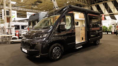 The Auto-Trail V-Line 610 Sport is black with two red striped decals its sliding door is open revealing its interior.