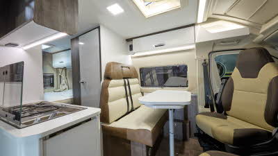 Benimar Benivan 144’s interior has brown and cream upholstery.  The furniture is brown and white.  The rear seats have seat belts.  The table can be extended and is folded.  There is a fixed bed to the rear.  The hob is on the left.  