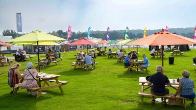 Visitors to The Great Caravan, Motorhome and Holiday Home Show sitting under bright umbrellas at picnic tables