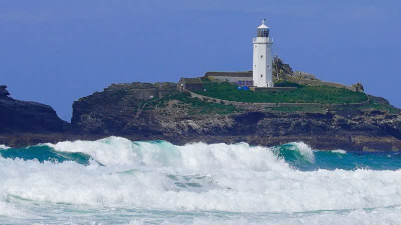 a white lighthouse looks out over the crashing waves and clear blue sea