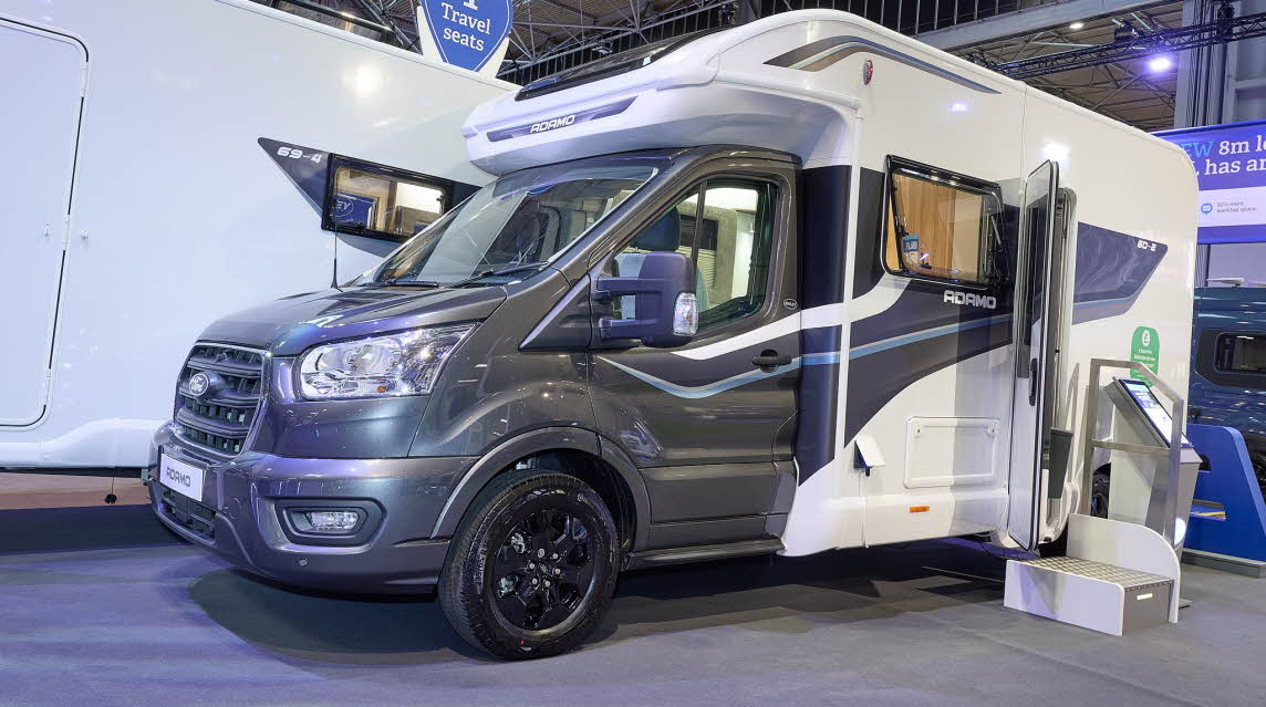 The Bailey Adamo 60-2 has a grey cab with a white body and has grey and blue decals.  There is a white and metal step by the habitation door.  There is an interactive stand to the right of the step. 