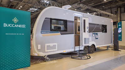 Buccaneer Starliner Barracuda has a grey exterior with a black decal with a teal and yellow strip under the window.  The entrance door is open and there is a black metal step to gain easy access to the interior.