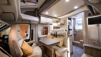 Benimar Mileo 243 Auto’s interior has beige and cream upholstery.  The furniture is wooden.  The rear seats have seat belts.  The table can be extended and is folded.  There is a fixed bed to the rear accessed by a wooden steps.  