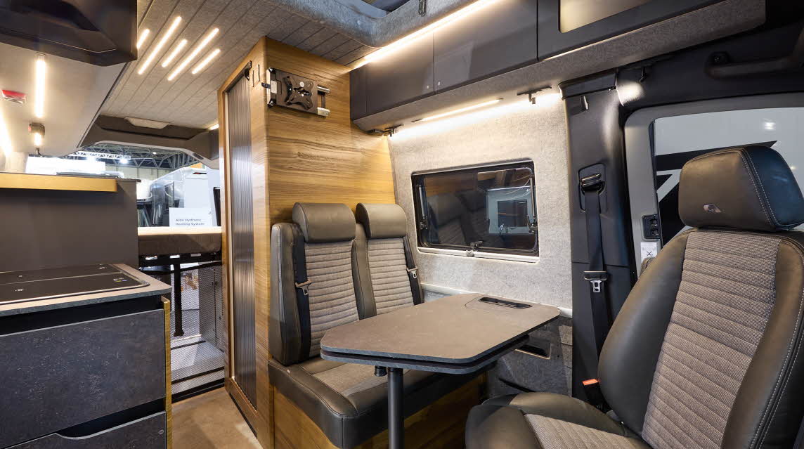 The Adria SuperTwin’s floor is wood effect limo, with dark grey cabinets and wooden panels.  The pop top roof is open and the ceiling is mid grey.  The upholstery is two tone with dark edging.  There is a grey table.