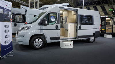 Auto-Trail Expedition 67 Flex's exterior is white with dark grey decals.  The sliding door is open revealing the lounge and kitchen.  There is a white step to gain easy access.