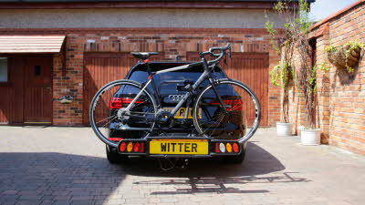 black car with witter number plate carrying bike on back
