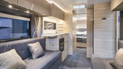 The Adria Altea 622 DP Dart has a front u shaped grey sofa with beige cushions.  The furniture is pale wood.  Towards the rear there is a fixed island bed.