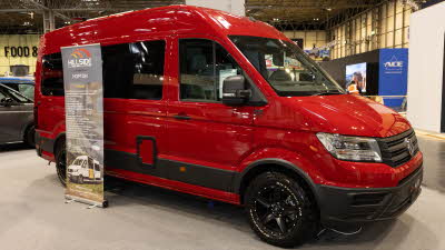 The Hillside Leisure Hopton 600RL is red.  There is a roller banner to the rear of the van.