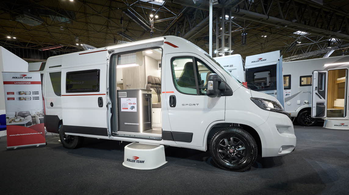 Roller Team Livingstone 6’s exterior is white.  It has grey and red decals.  The habitation door is open revealing the seating area and there is a large white step to gain easy access.