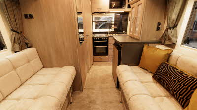 The Auto-Sleeper Nuevo EK Plus has cream upholstery, the furniture is wooden and there is a beige removable carpet on the floor.  There is a microwave above the sink.