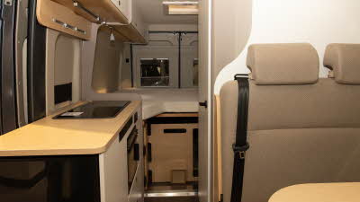 The Elddis Whirlwind GTV 563 has fawn upholstery, the kitchen is to the left with a rear fixed bed.  The cabinets are cream with a wooden panel underneath.
