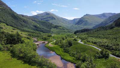 A view from above looking down over the river with is flowing between the grassy mountain slopes 
