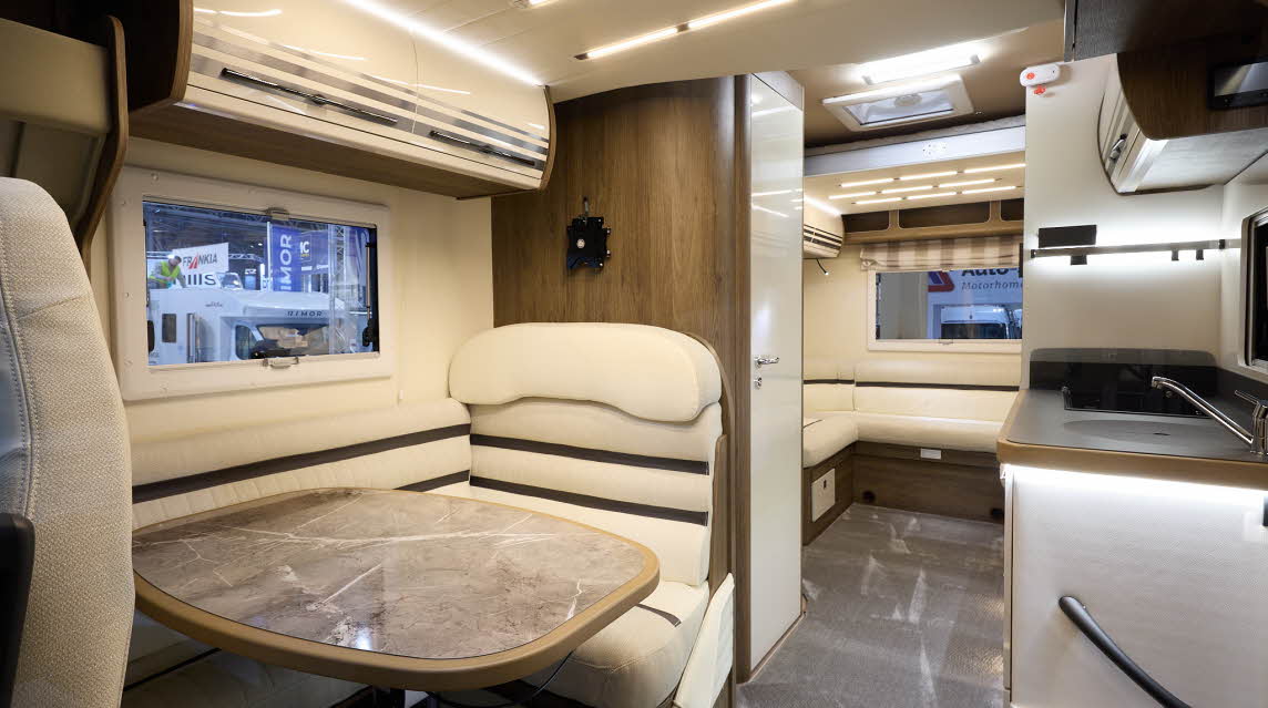 The Roller Team T Line 700 has grey carpet.  The upholstery is cream with dark brown highlights.  There is a marble effect table in front of the sofas.  The cabinets are cream with wooden surrounds.  There is a rear lounge.
