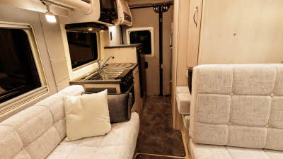 The Auto-Sleeper Symbol has pale upholstery and there are two cushions on the sofa.  There is brown removable carpet on the floor.  The kitchen is situated towards the rear.