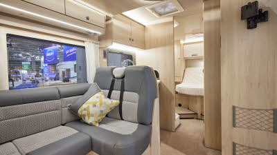 Auto-Trail F-Line F74 has two tone upholstery, with pale wooden furniture.  The floor has beige carpet.  To the rear is a fixed bed which is designed to lift the mattress at the top.  