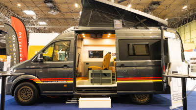 Out and About Campers Summit is grey and has a red and yellow striped decal.  Its rising roof and sliding door are open.  There is a step to enable easy access.