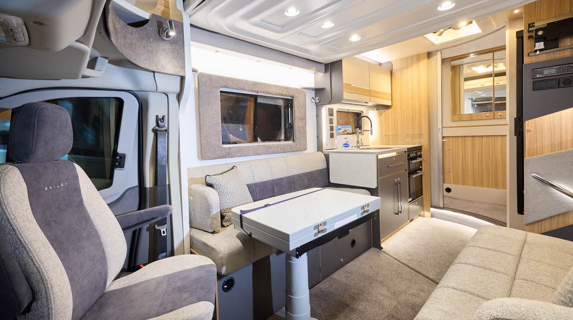 The Bailey Adamo 69-4 has beige carpets, with cream and pale wood cabinets.  The upholstery is cream and dark brown.  There is a step to the rear washroom.  There is a folded table in front of one of the sofas.