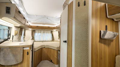 Eriba Touring 542 Legend’s interior has wooden furniture and there is a fixed bed to the rear.  The pop top roof is extended with a white canvas surround.  The handles and wall hooks are black.