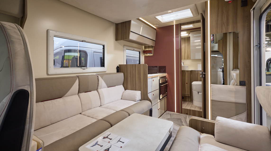 The Roller Team Kronos Compact 590 has grey carpet.  The upholstery is cream and mid brown.  The cabinets are cream with wooden surrounds and the interior door is a dark brown.  There is a step up to the rear washroom.