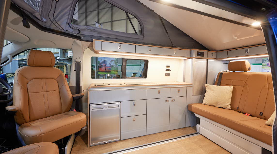 Ecowagon Expo+ has tan leather upholstery, silver kitchen units and a fridge. It has a wooden effect floor and there is a sliding rail to move the rear travels seats backwards or forwards easily. 
