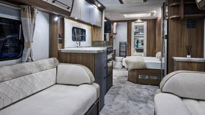 Interior of the Buccaneer Starliner Cruiser with cream sofas edged with suede effect material.  The fixed bed is next to the kitchen and the door to the rear washroom is open.  The large windows and two skylights will let natural light flood in.