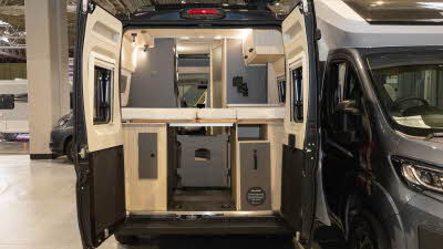 The Xplore CV X9 has pale wooden cabinets, the rear doors are open revealing the fixed beds which has further cupboards and storage under the bed.