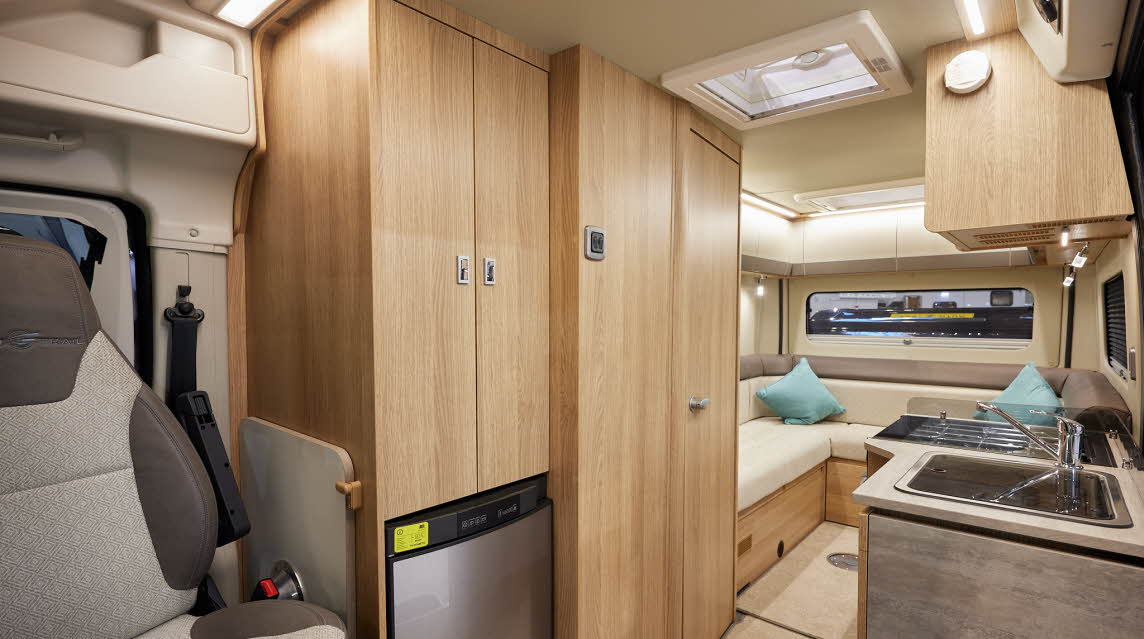 Auto-Trail V-Line 610 Sport has cream upholstery, with wooden furniture.  The floor has beige carpet.  The overhead lockers are cream.  The kitchen has a square sink and a flap to extend kitchen work surface.  The vehicle has a rear lounge.