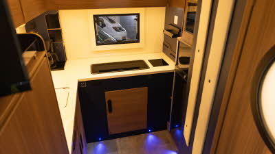 The Rimor Sailer Plus 56 has a rear kitchen.  The cabinets are wooden with brown accents.  There is a rear window behind the sink and hob.