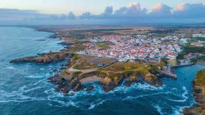 A view from above the sea looking back over the rugged coastline and buildings or Porto Covo