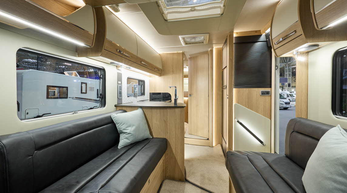 Auto-Trail Grande Frontier GF-80's interior has brown leather upholstery with pale grey cushions.  The furniture is wooden and it has two skylights.  The rear internal door is open revealing the bedroom.