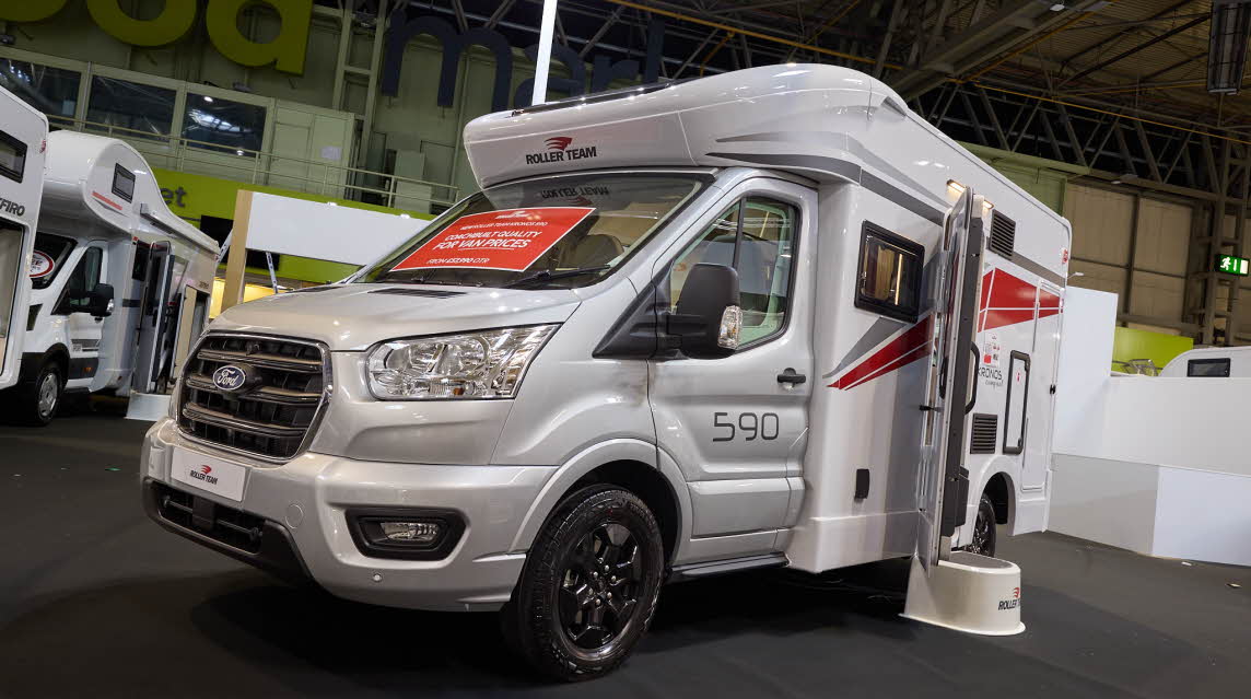 The Roller Team Kronos Compact 590 has a silver cab and white body with grey and red decals.  There is a white step outside the open habitation door. 