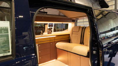 The Out and About Campers Alpine Tourer has beige upholstery and has brown and wooden cabinets.