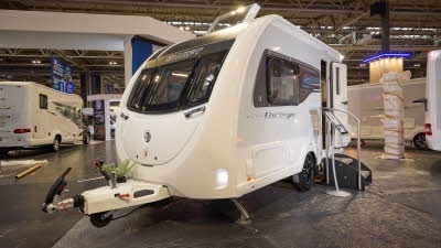 Swift Challenger 390 is white with grey sides.  Its entrance door is open and there are two steps for easy access.  There is a display stand next to the steps.