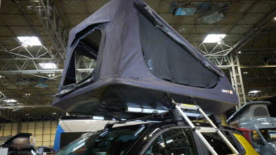 The TentBox GO is shown on a yellow jeep.  Its canvas is grey with black windows.  There is a silver ladder.
