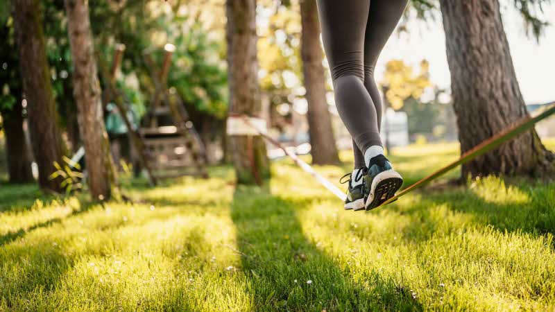 feet in leggings and trainers walks along a low slackline through the trees