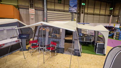 The Camp-Let Earth has a cream canvas roof. It has a separate annex for the kitchen. There are two red camping chairs under the canopy. The doors are open revealing the bedroom and kitchen units.