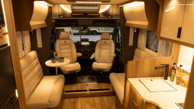 The Coachman Travel Master 545 has cream leather upholstery. The two front seats are swivelled to face into the van and there is a round cocktail table on the left.