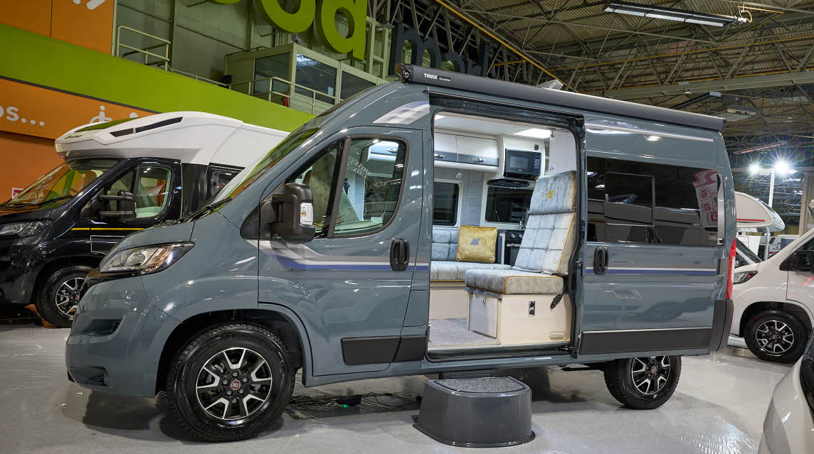 Auto-Sleeper Symbol's exterior is mid grey, the entrance door is open and there is a step to gain easy access.  Its sliding door is open revealing the lounge.