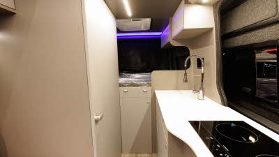 The Bespoke Leisure Bespoke Edition Volkswagen Crafter has white doors and cabinets, there is a rear fixed bed.  The kitchen with an induction hob is to the right.