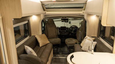 The Elddis Avalon 255 with XT Pack has dark brown upholstery complemented with pale wooden furniture and cream cabinet doors.  The kitchen sink is in the bottom right corner.  The two front seats are facing into the van.