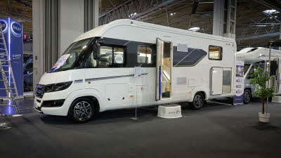 Auto-Trail Grande Frontier GF-80's exterior is white with dark blue and black decals.  The entrance door is open revealing a handrail and there is a white step to gain easy access.  There is a roller banner to the rear.