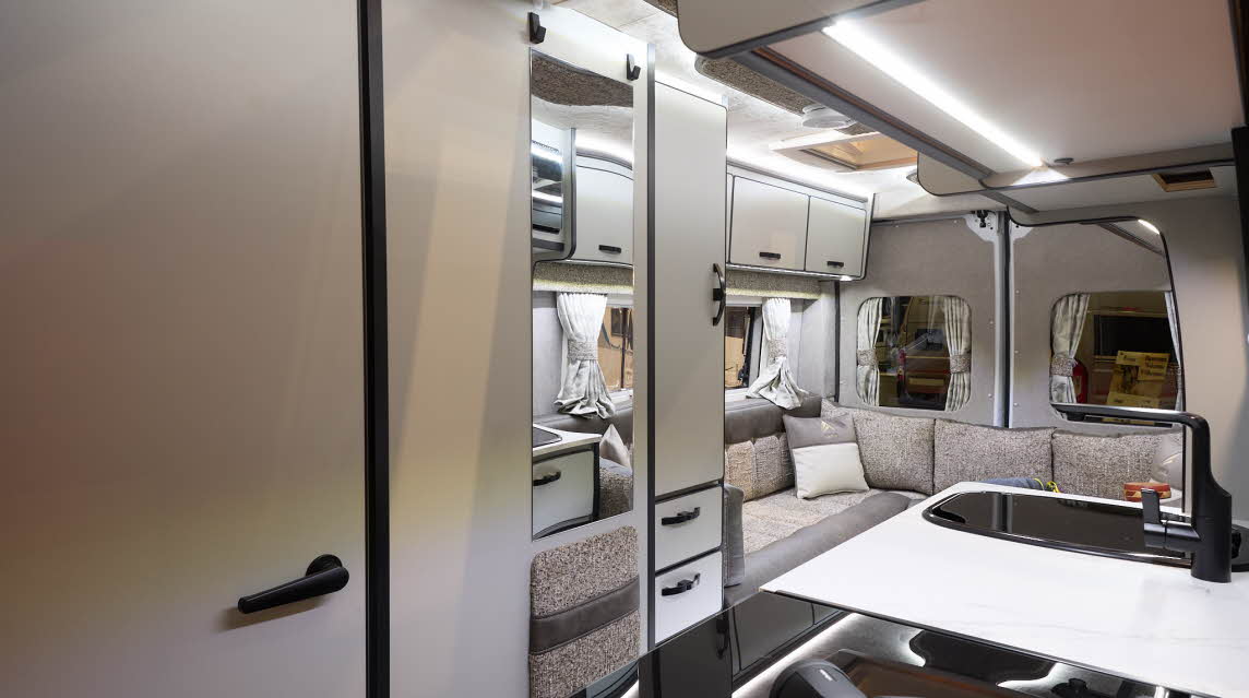 The Aura Campervans 7 EL has a rear lounge.  The upholstery is pale and dark brown.  The cabinets are cream.  There is a hob in the front.  