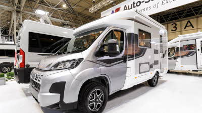 The Auto-Sleeper Nuevo EK Plus has a silver cab and a white coachbuilt body.  It has grey and black stripe decals along the side.