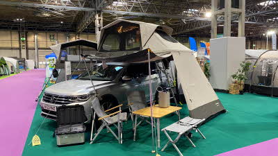 Dometic TRT 140 Air has a khaki exterior and is shown on top of a silver car.  There is a large outside area under the tent's platform with a table and chairs