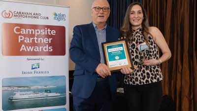 A Caravan and Motorhome Overseas Campsites Award Winner with the Chairman next to a sign showing Campsite Partner Awards, with Irish Ferries below it